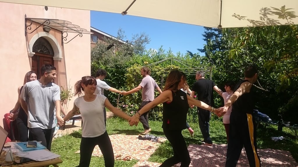 a group of people holding hands and dancing in a garden, classe di bioenergetica