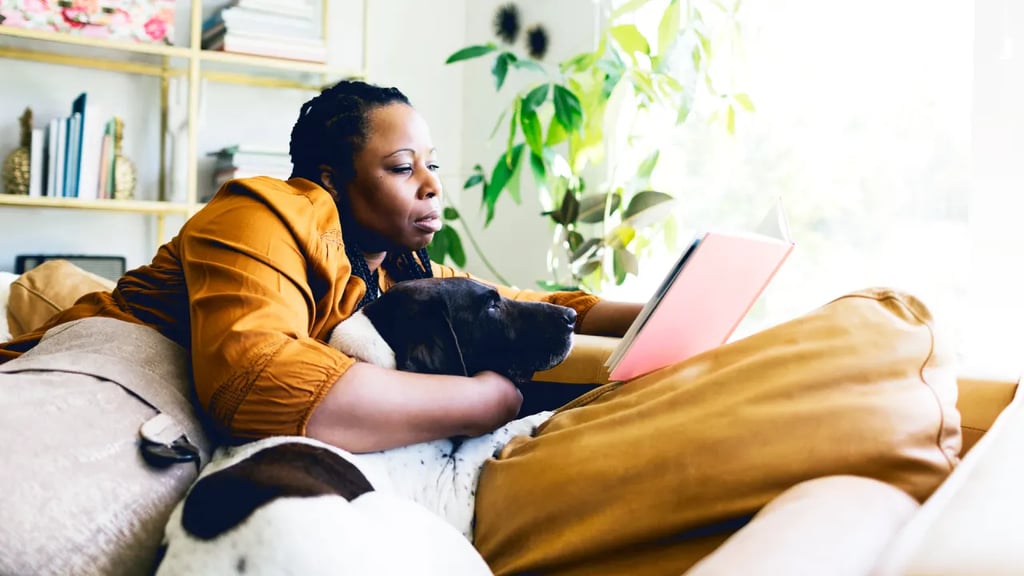 Una mujer afro sentada en un sofá con un perro y leyendo