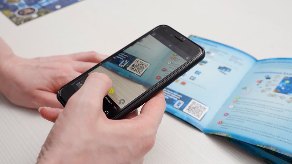 Telefonu skenuojamas QR kodas nuo žaidimo taisyklių knygelės