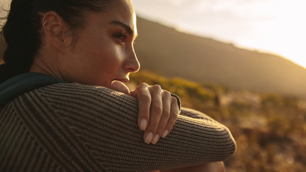 A woman in a knit sweater looking at a mountain sunset during a nature hike.