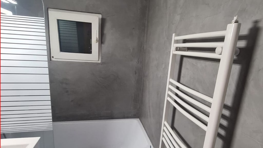 Modern bathroom with grey microcement walls, a white bathtub, and a heated towel rail.