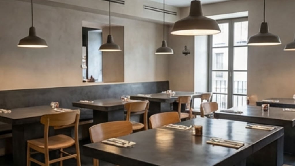 Modern, minimalist restaurant interior with microcement walls and tables, featuring industrial penda