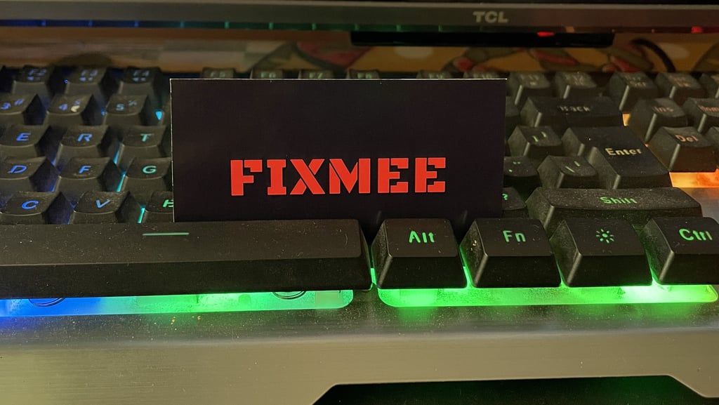 A FIXMEE business card placed on an RGB backlit gaming keyboard with green and blue LED lights.