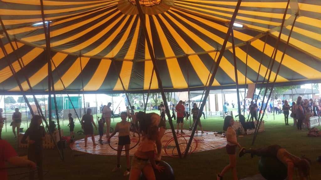 Children participating in a circus skills workshop inside a yellow and black striped marquee tent..