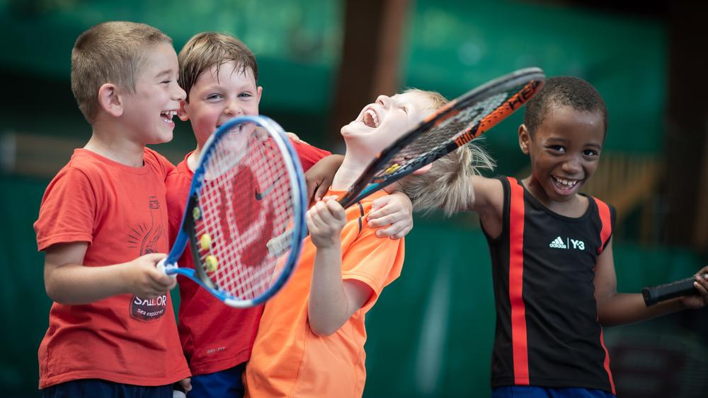 Image avec des enfants qui rigolent et tiennent des raquettes de tennis