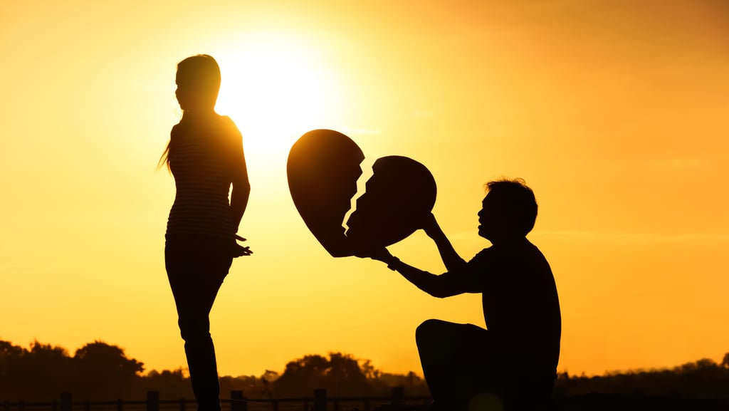 Um homem segurando um coração partido para uma mulher que esta de costas para ele