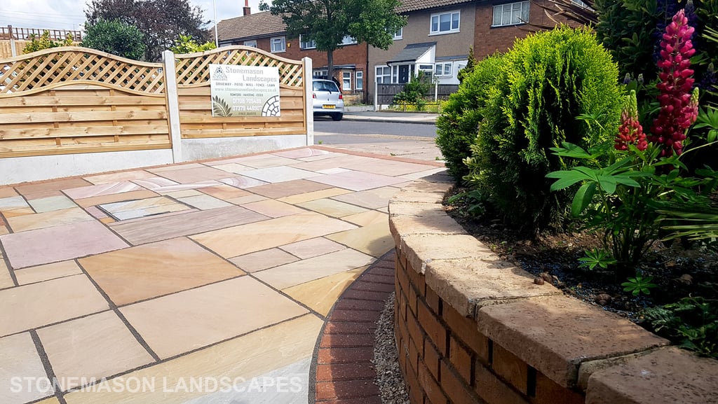 Colourful sandstone paving driveway and curved raised planter with colourful plants and flowers