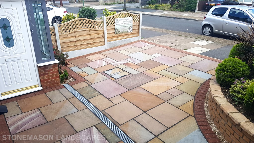 Colourful sandstone paving driveway and curved raised planter with colourful plants and flowers