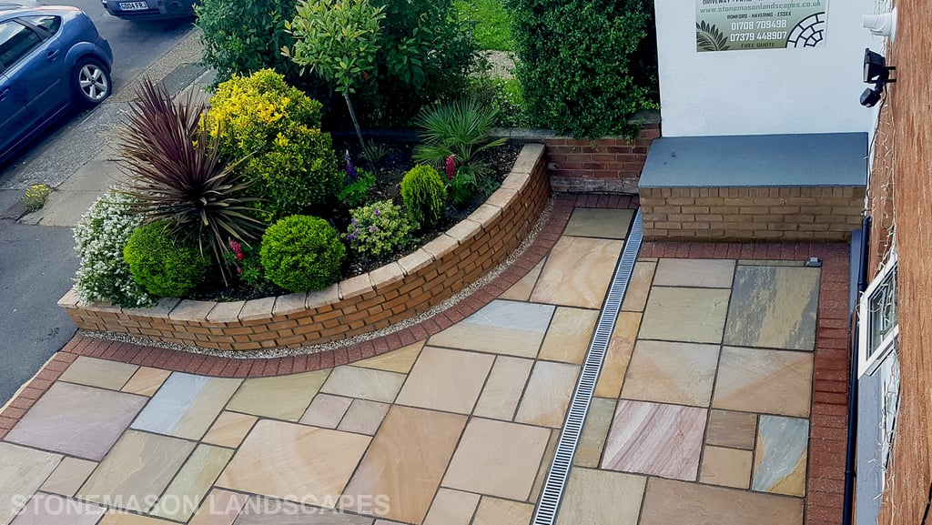 Colourful sandstone paving driveway and curved raised planter with colourful plants and flowers