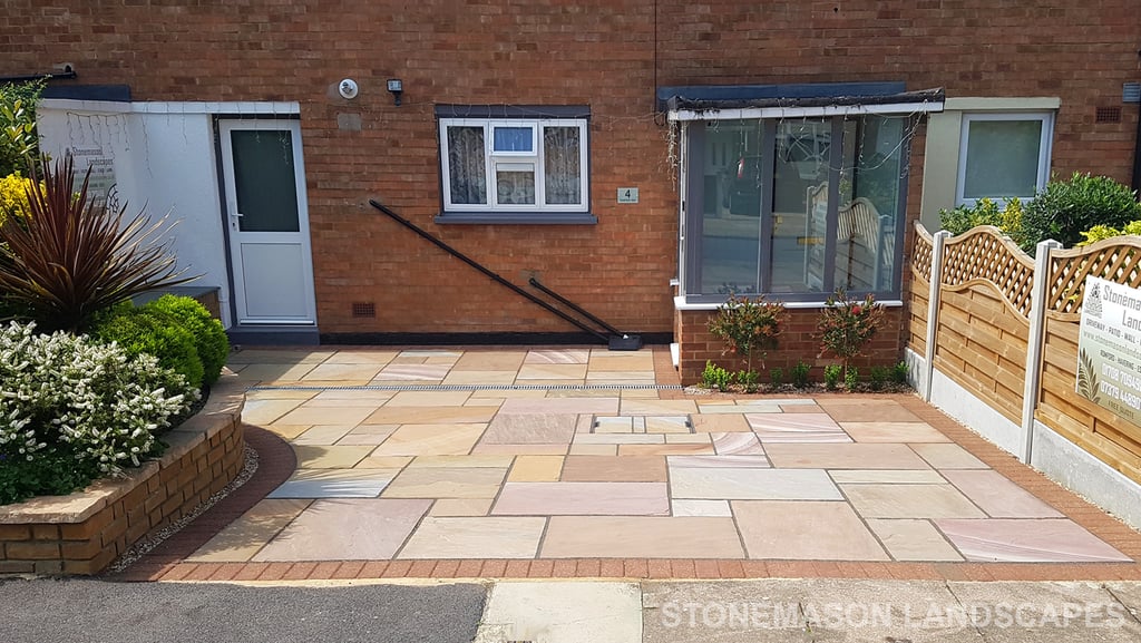 Colourful sandstone paving driveway and curved raised planter with colourful plants and flowers
