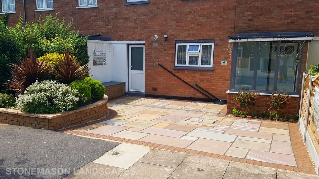 Colourful sandstone paving driveway and curved raised planter with colourful plants and flowers