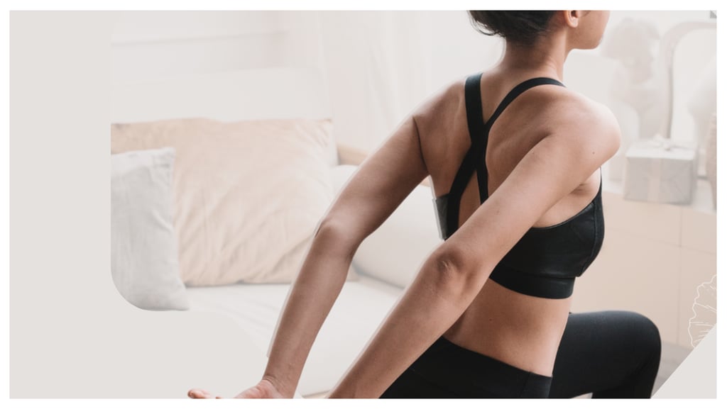 A woman in a black sports bra performing a chest and shoulder stretch in a bright living room.