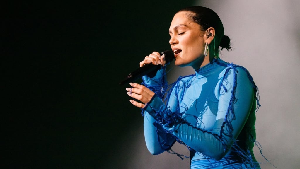 Jessie J cantando no palco, segurando um microfone e usando um traje azul.