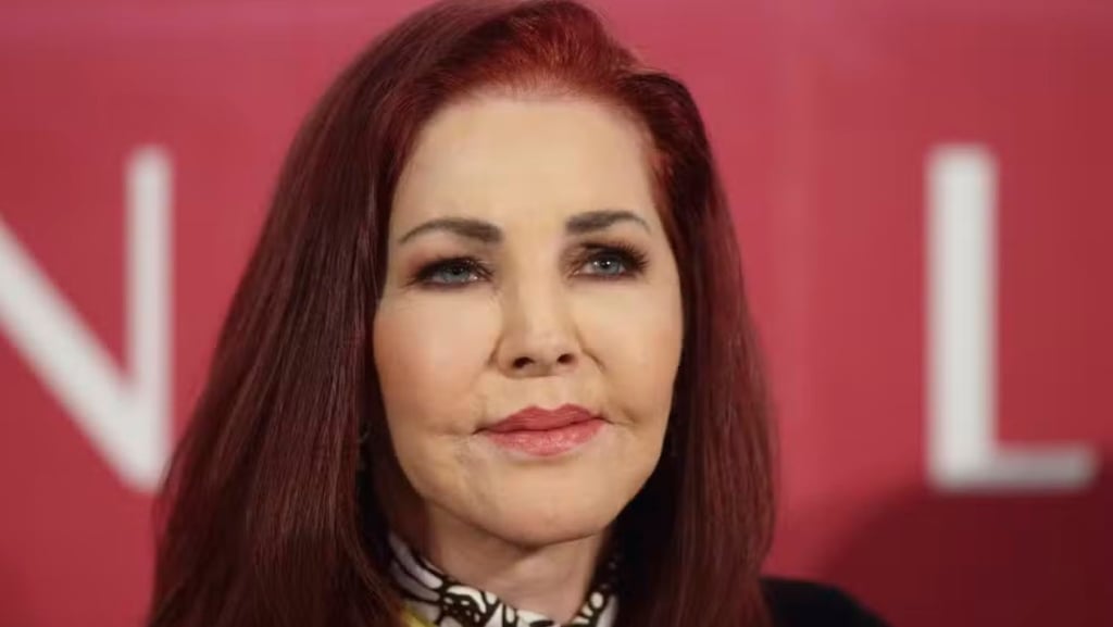 Priscilla Presley com cabelo ruivo e olhos azuis, olhando para a câmera.