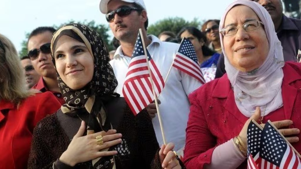 Mulheres muçulmanas sorrindo com bandeiras americanas, em uma cerimônia de cidadania.