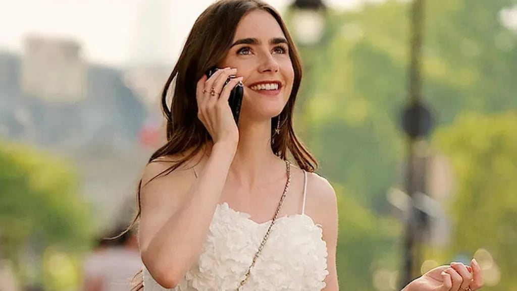 Lily Collins sorrindo e falando ao telefone, vestida de branco em Paris.