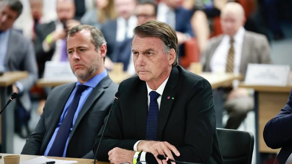 air Bolsonaro sentado em uma mesa, com outros participantes de uma reunião.