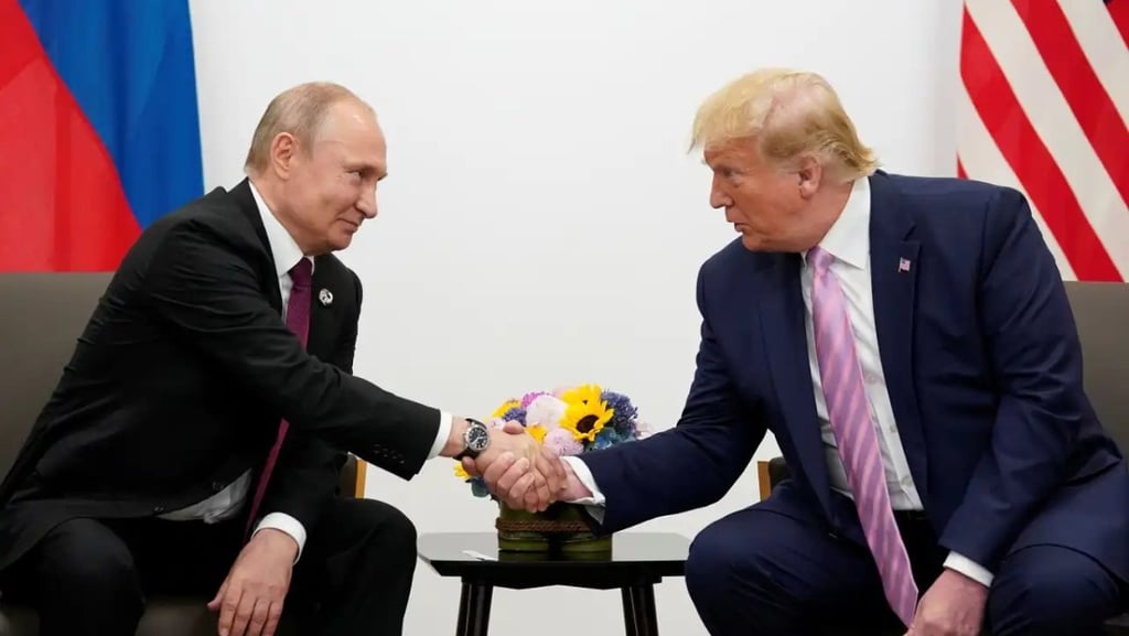 Donald Trump e Vladimir Putin se cumprimentam na frente de bandeiras.