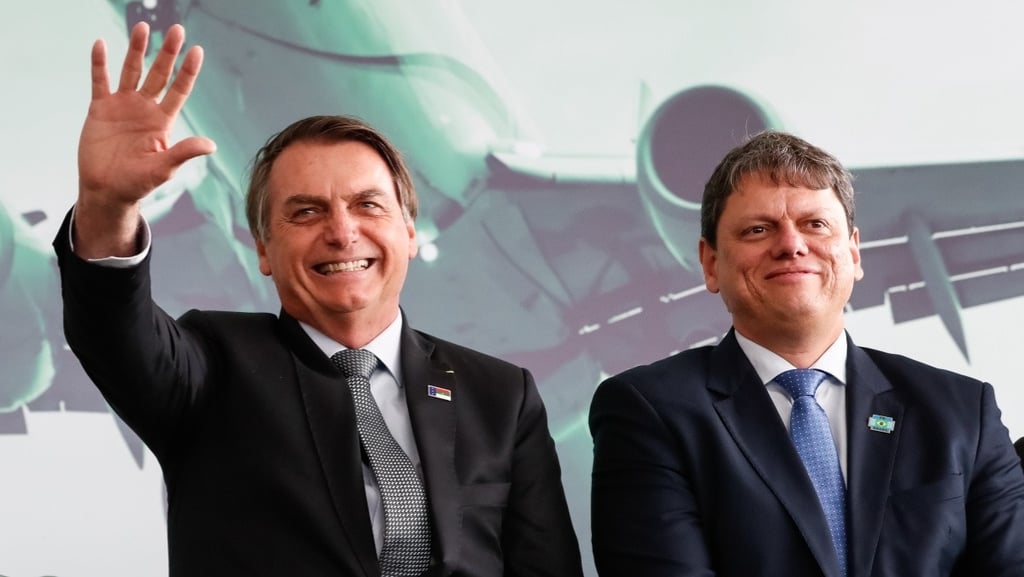 two men in suits and ties standing in front of a large screen