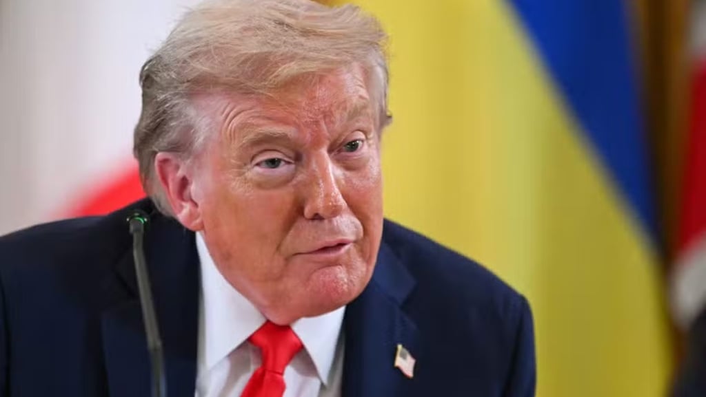 Close de Donald Trump com gravata vermelha, falando em uma mesa.