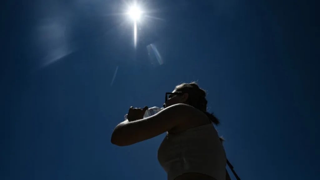 Silhueta de uma pessoa bebendo água sob o sol forte em um dia de calor.