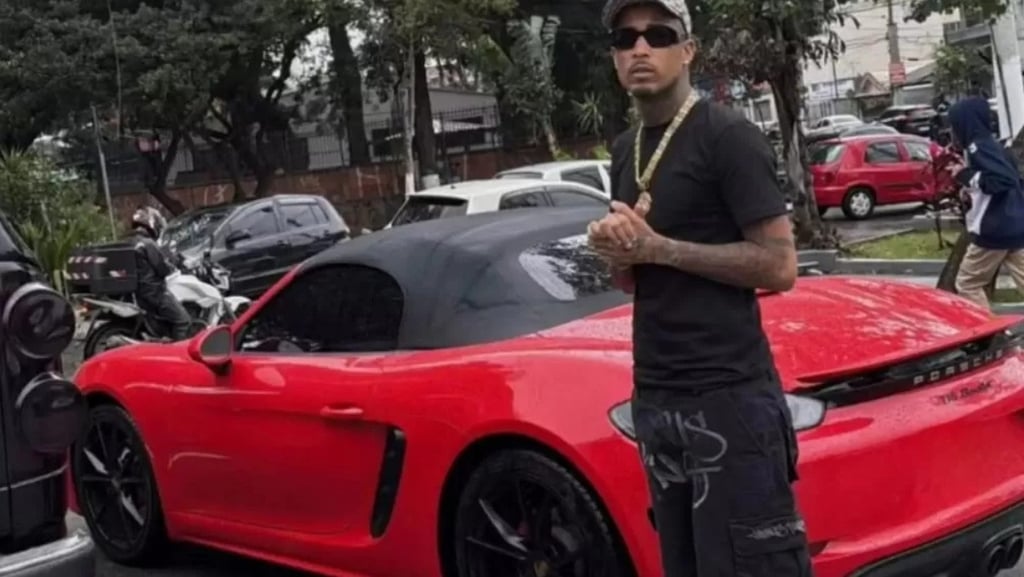 a man in a black shirt and sunglasses standing next to a red sports car
