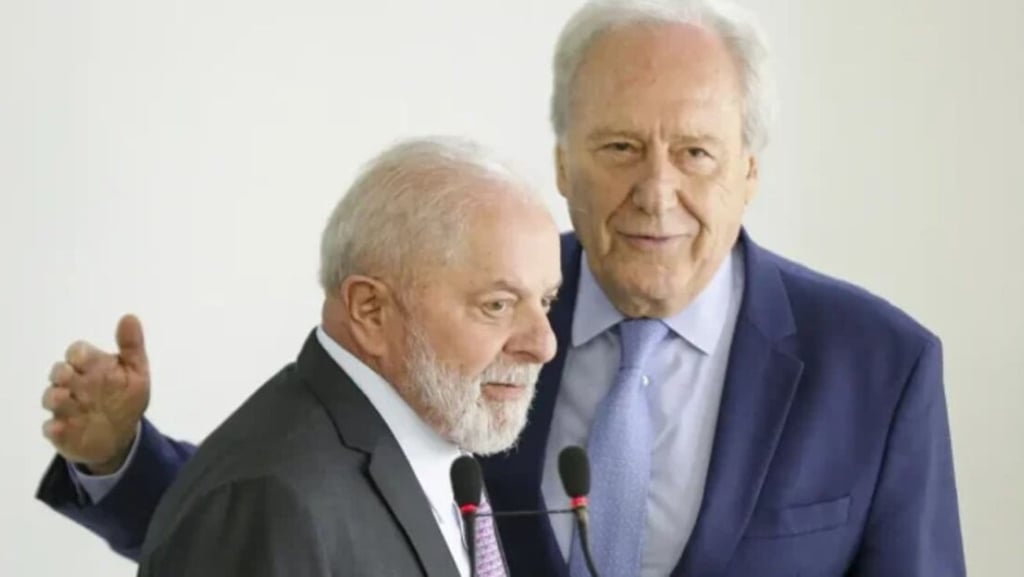 Lula com um microfone, ao lado de um homem mais velho, em um evento formal.