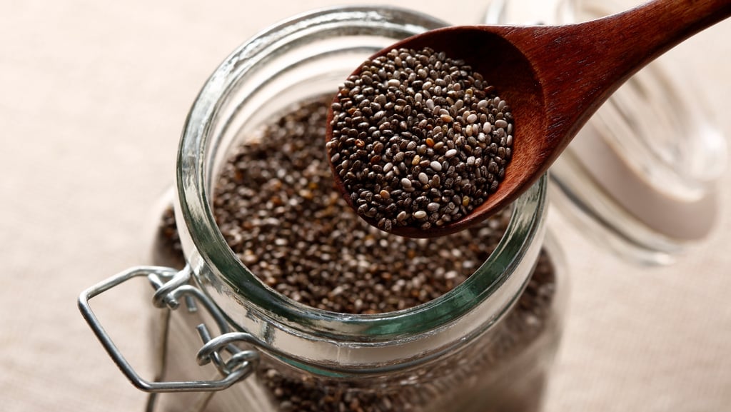 Jar of chia seeds with a wooden spoon scooping out a serving size to show portion and texture.