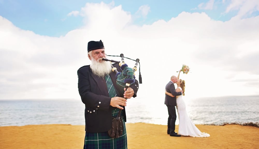couple kissing on bluff at Sunset Cliffs with bagpiper in forground