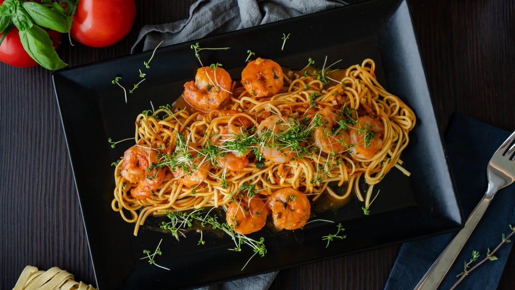Spaghetti mit Garnelen in Tomatensauce und frischen Microgreens auf schwarzem Teller.