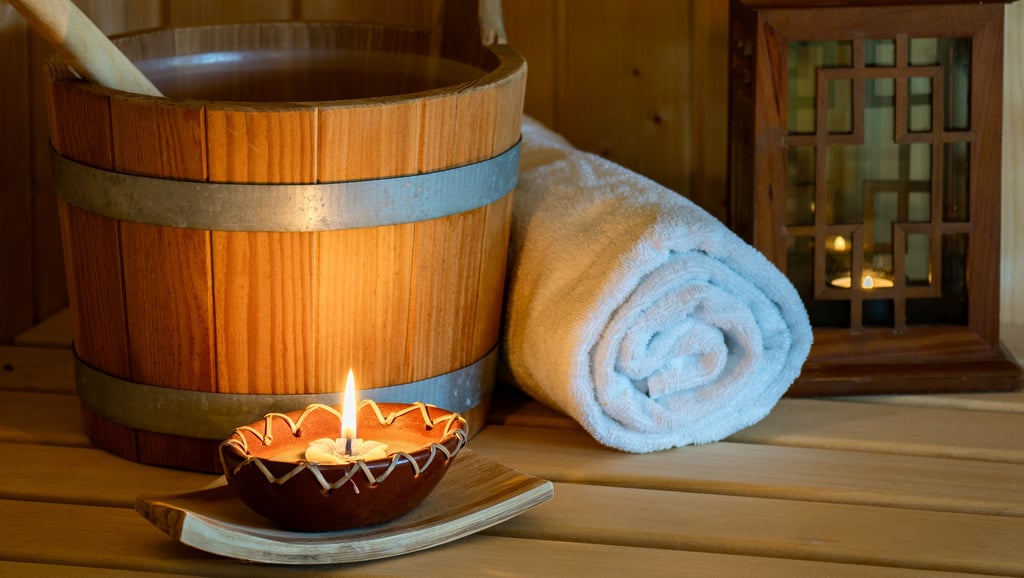 Wellness-Sauna mit Holzeimer, gerolltem weißen Handtuch und stimmungsvoll brennender Kerze.