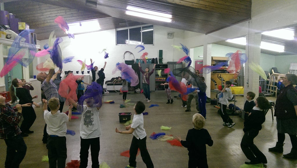 Children and adults throwing colourful juggling scarves in a vibrant indoor sensory workshop.
