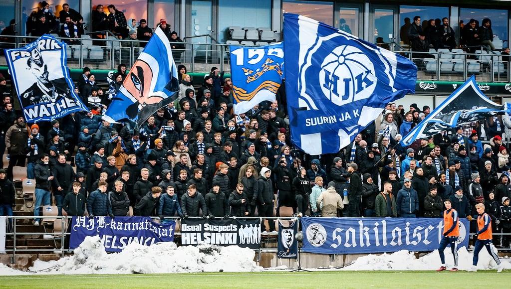 Fans von HJK Helsinki feiern in der Bolt Arena, mit blau-weißen Schals, Tribünen im Hintergrund und lebendiger Stadionstimmun