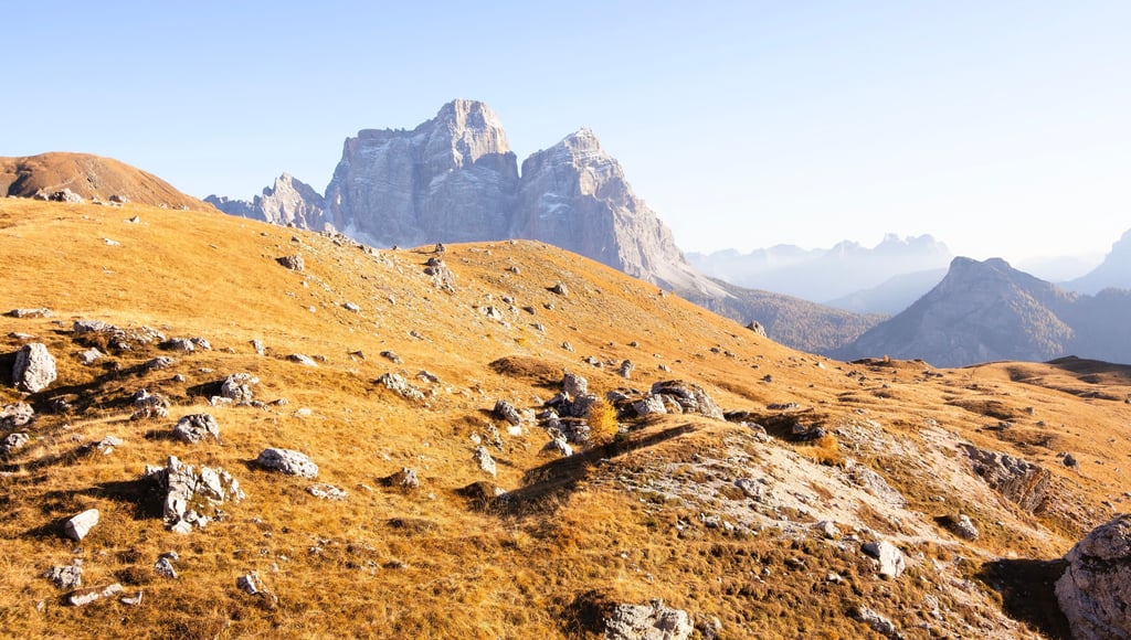 Golden autumn meadows and rocky slopes in the Italian Dolomites under a clear blue sky.