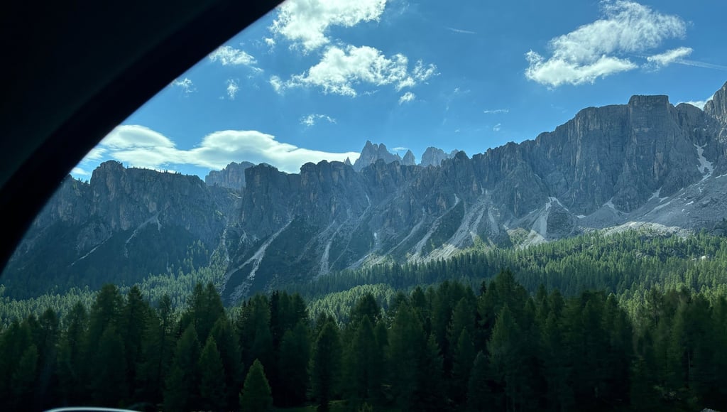 Scenic view of the jagged Dolomite mountains and pine forests in Italy from a car window.