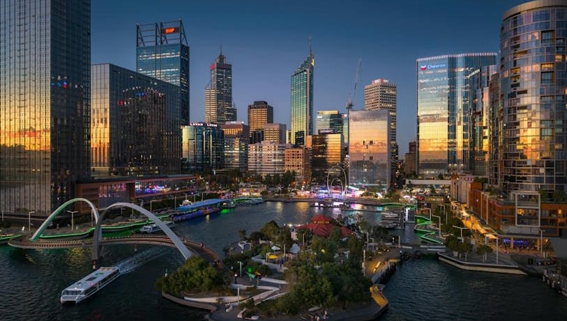 city skyline at sunset, featuring Quay and River with illuminated buildings and a pedestrian bridge