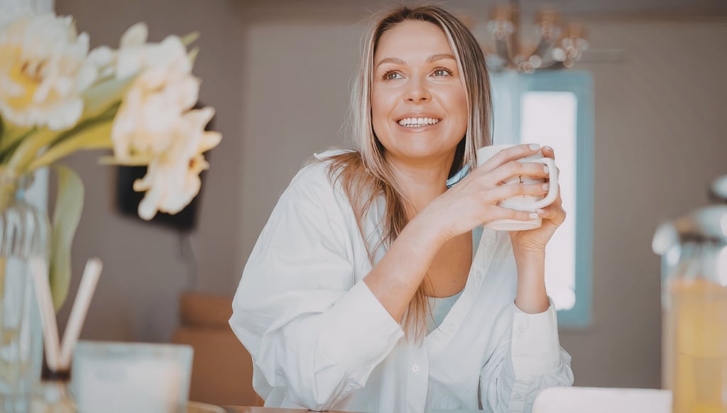 Smiling woman in a white shirt holding a coffee mug during a relaxed morning at home.