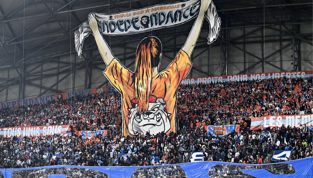 Jubelnde Marseille-Fans im Stadion, umgeben von Fahnen, Rauch und lautstarker Atmosphäre.
