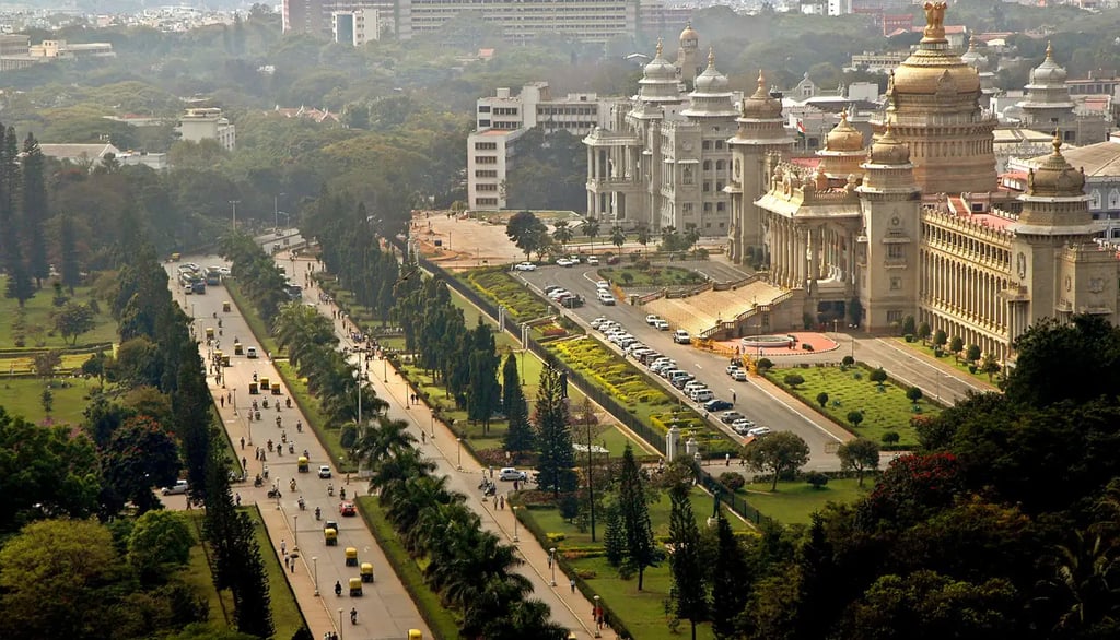 Aerial view of a city featuring a road lined with trees, surrounded by buildings and green grass, sh