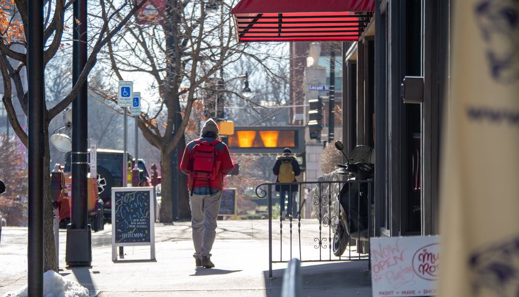 Man walking on a sidewalk downtown past business and sandwich signs