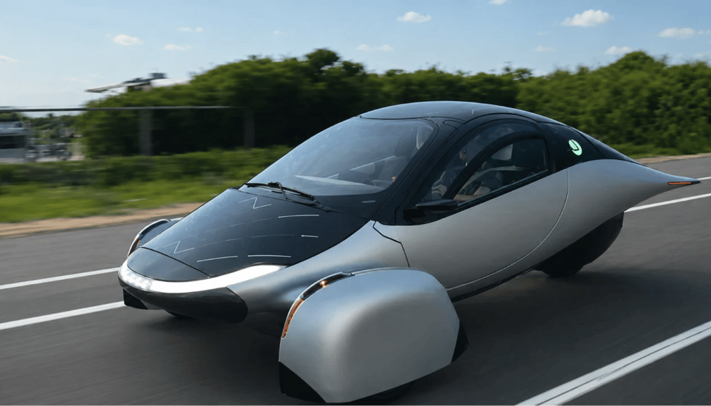 Aptera Solar EV rodando em rodovia durante o dia com carroceria aerodinâmica e painéis solares