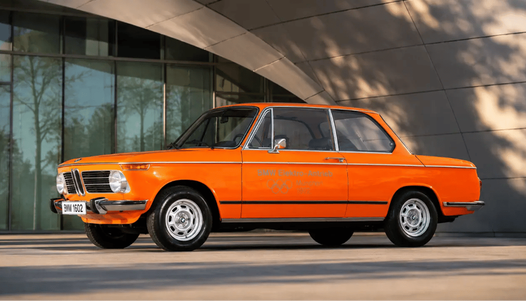 BMW 1602e de 1972 exposto diante de arquitetura moderna em imagem histórica