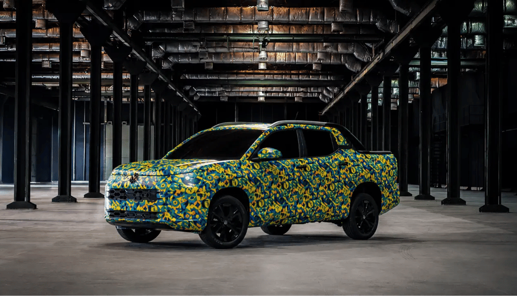 Nova picape VW Tukan camuflada exibida em galpão industrial com iluminação dramática.