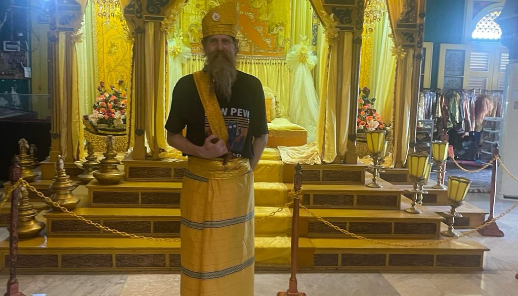 a man at Istana Maimun in traditional Indonesian ceremonial hat and sarong with a kris