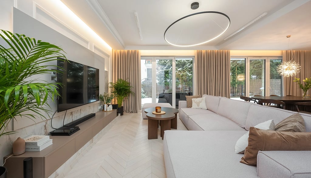 Nowoczesny salon z jasną sofą, stolikiem kawowym, telewizorem na ścianie i dużymi oknami