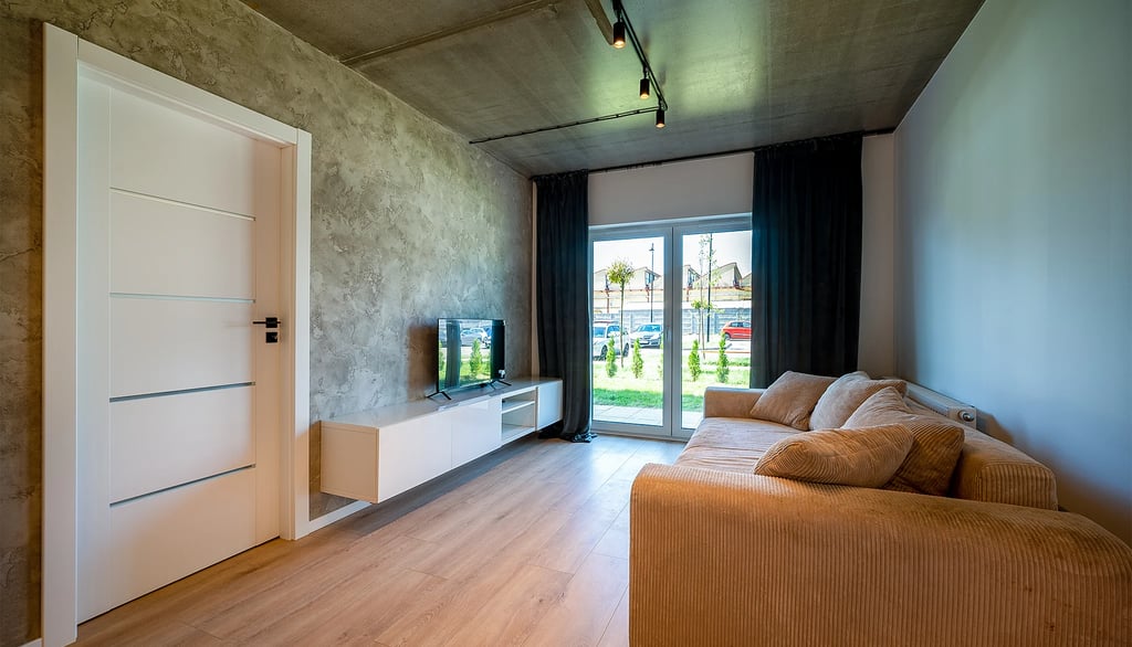 Salon z beżową sofą, szafką RTV z telewizorem, drzwiami i oknem tarasowym