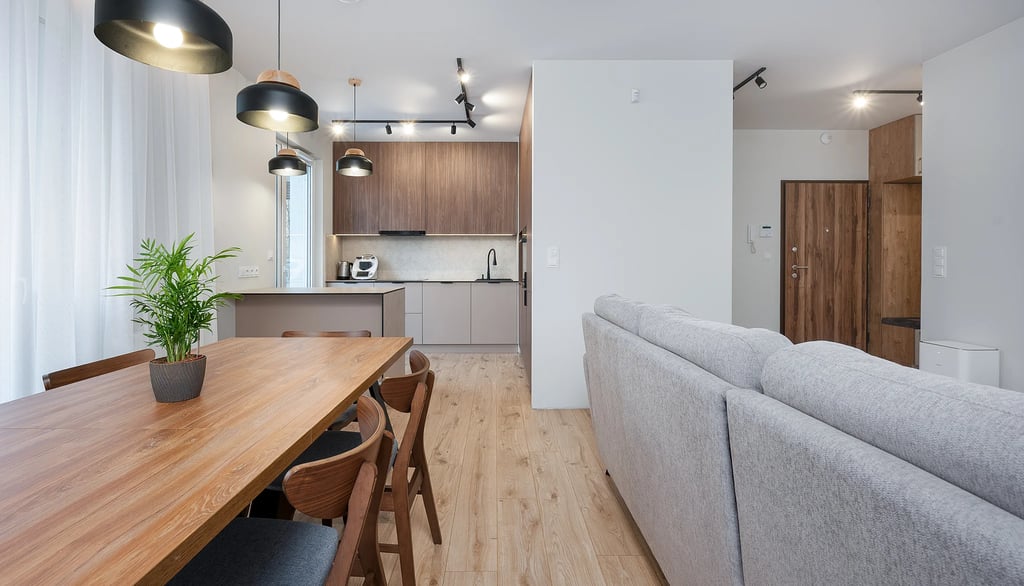 Nowoczesny salon z aneksem kuchennym, drewniany stół, sofa i wyspa kuchenna.