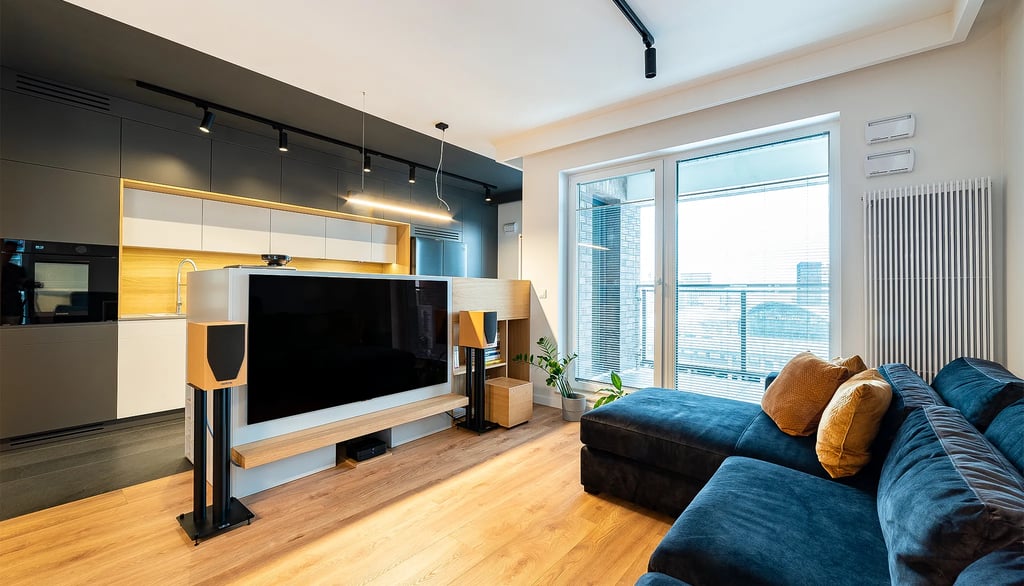 Nowoczesny salon z aneksem kuchennym, sofą, telewizorem i zestawem audio. Duże przeszklenia