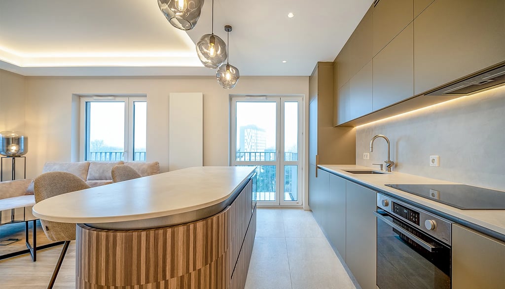 Kuchnia z wyspą, zabudową AGD, oświetleniem sufitowym oraz dużymi oknami balkonowymi.