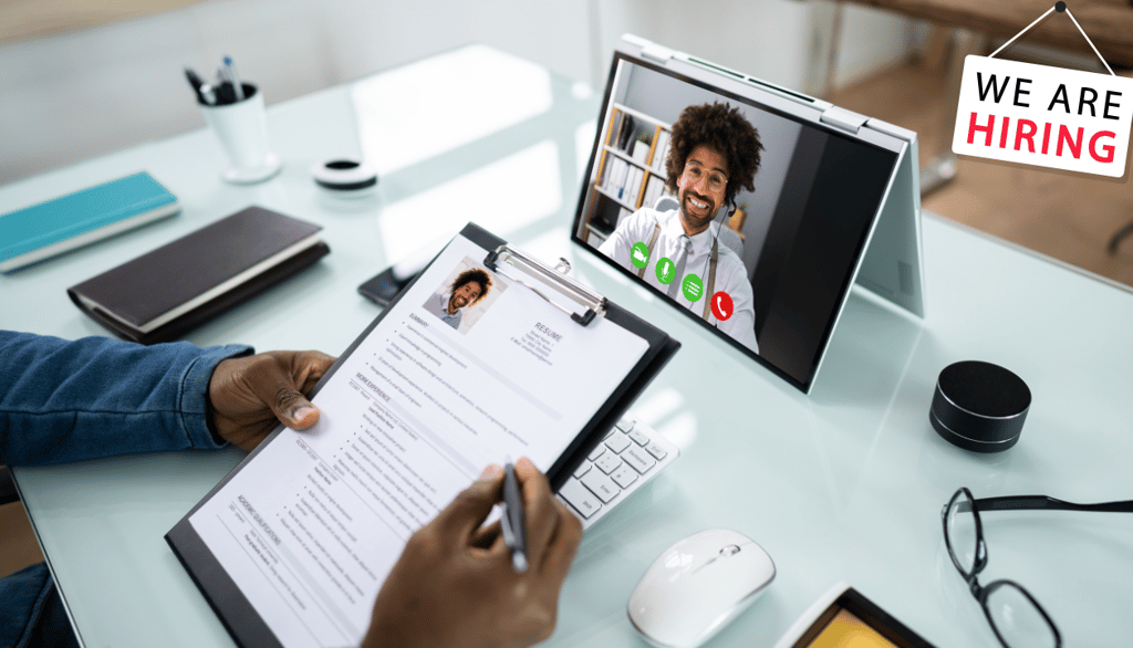a person sitting at a desk with a tablet conducting an online job video interview with a guest